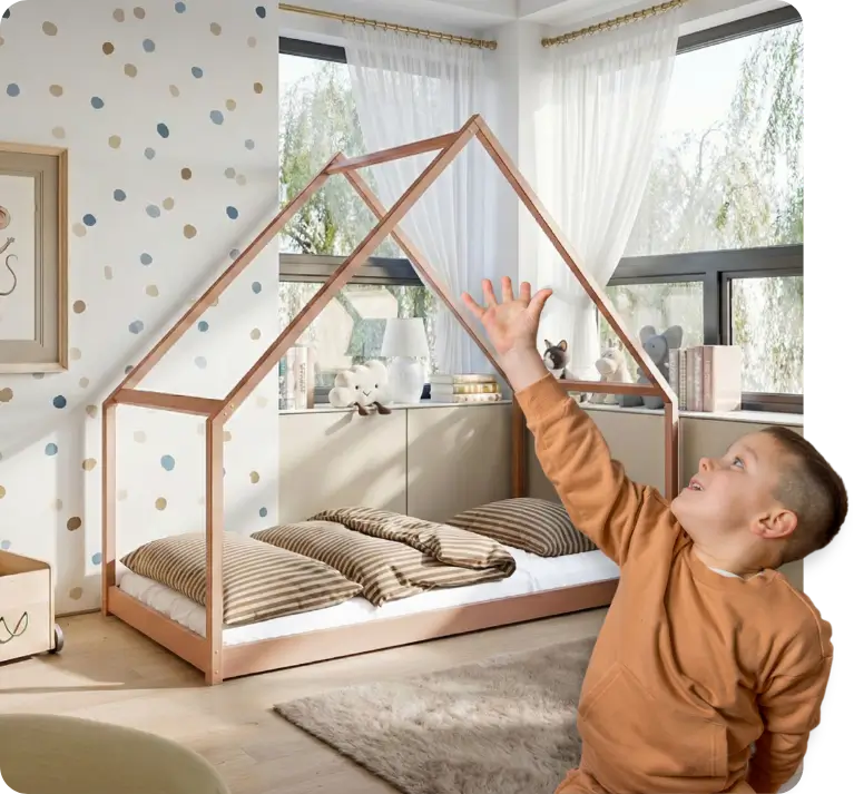 En pojke visar en säng i kanelfärg formad som ett hus bakom sig.